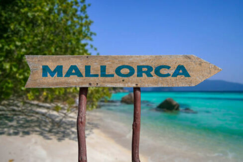 Mallorca wooden arrow road sign against beach with white sand and turquoise water background. Travel to Mallorca concept.